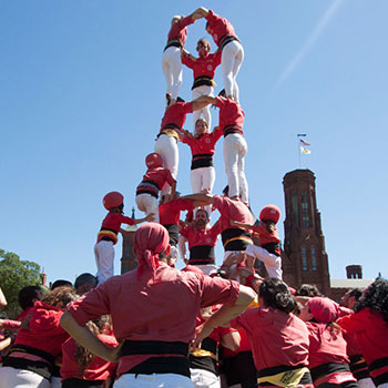 Several adults and children dressed in red shirts and white pants form a human tower in front of the Smithsonian Castle.